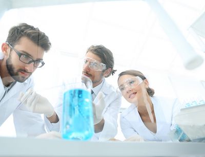 Drei Personen in Laborkitteln beobachten ein Becherglas mit blauer Flüssigkeit